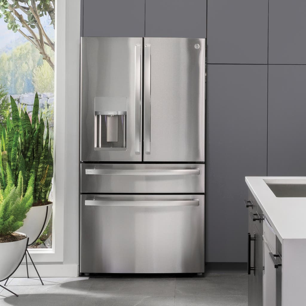 Stainless steel refrigerator in a modern kitchen with gray walls and a window view.
